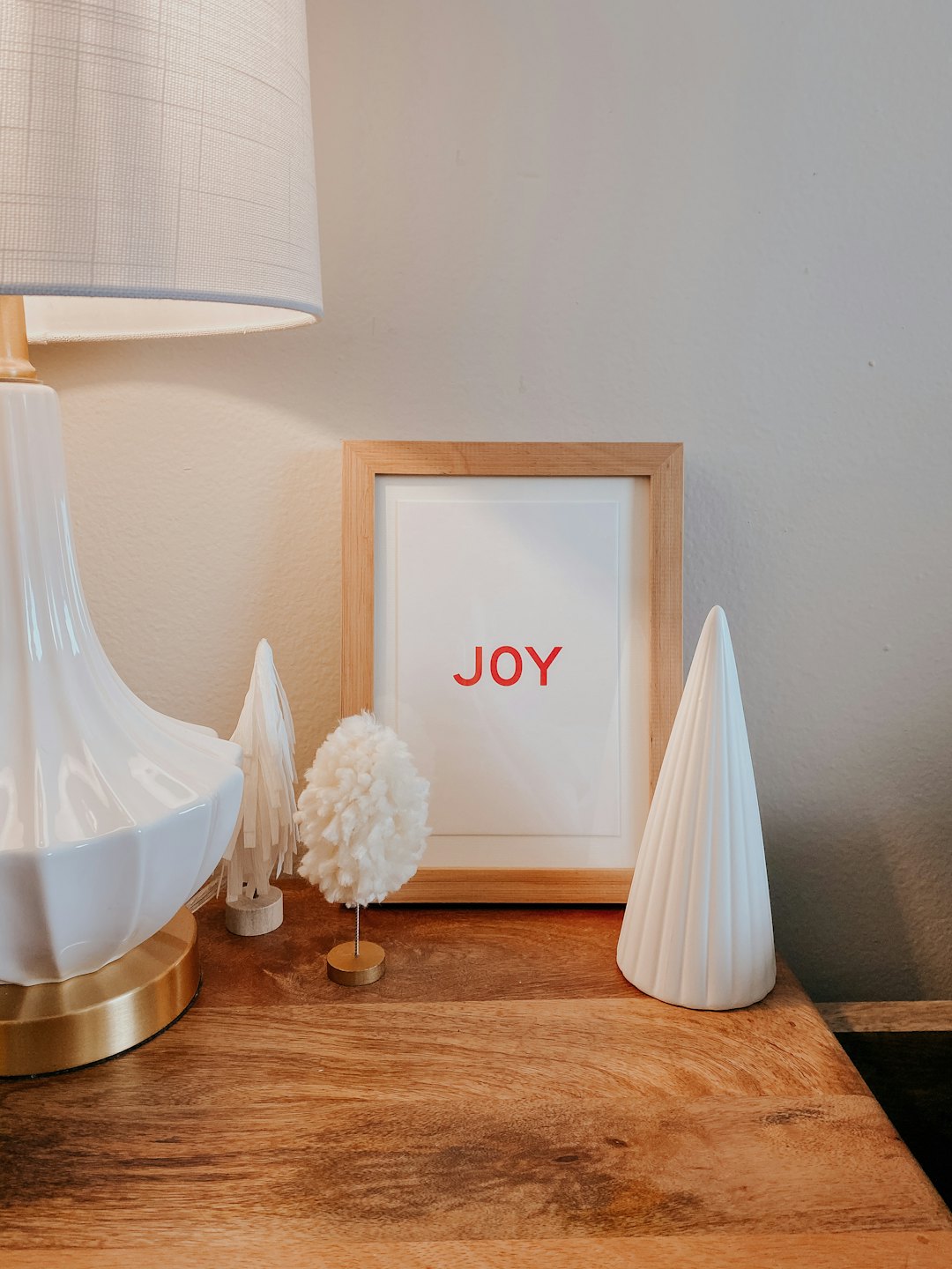 Minimalistyczne świąteczne dekoracje, w tym lampa i napis JOY na drewnianym stole.